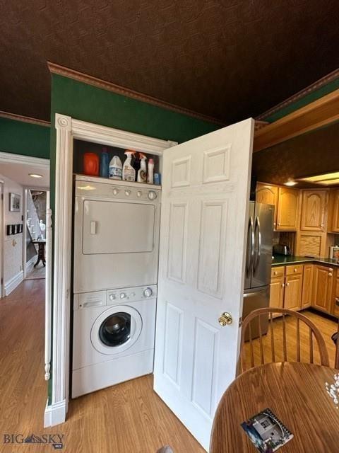 laundry area with ornamental molding, wood finished floors, stacked washer / dryer, and laundry area