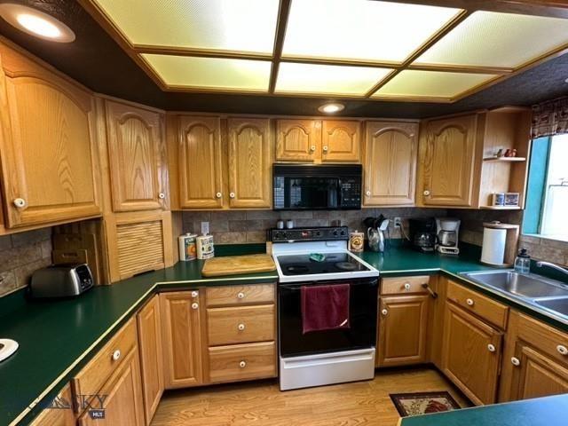 kitchen with a sink, black microwave, light wood-style flooring, dark countertops, and electric range