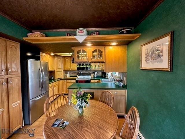 kitchen featuring stove, a sink, dark countertops, freestanding refrigerator, and glass insert cabinets