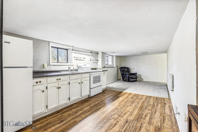 kitchen featuring white appliances, a sink, dark countertops, white cabinets, and wood finished floors