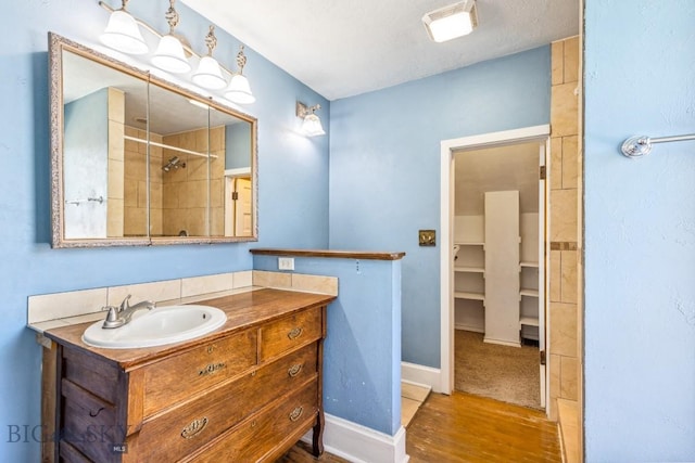 bathroom with vanity, a tile shower, baseboards, visible vents, and wood finished floors