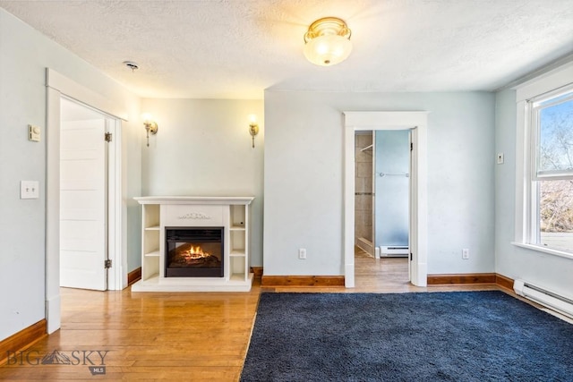 unfurnished living room with a textured ceiling, a glass covered fireplace, baseboard heating, and wood finished floors