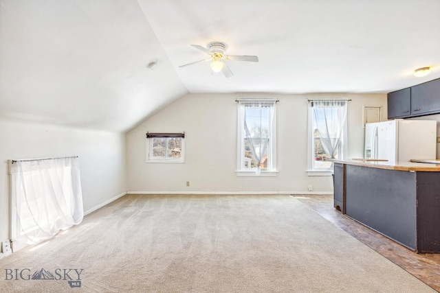 interior space with baseboards, lofted ceiling, ceiling fan, and light colored carpet