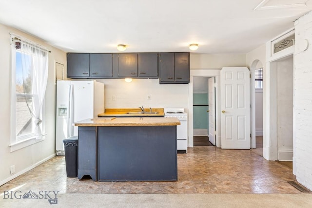 kitchen with light countertops, white appliances, baseboards, a kitchen island, and a sink
