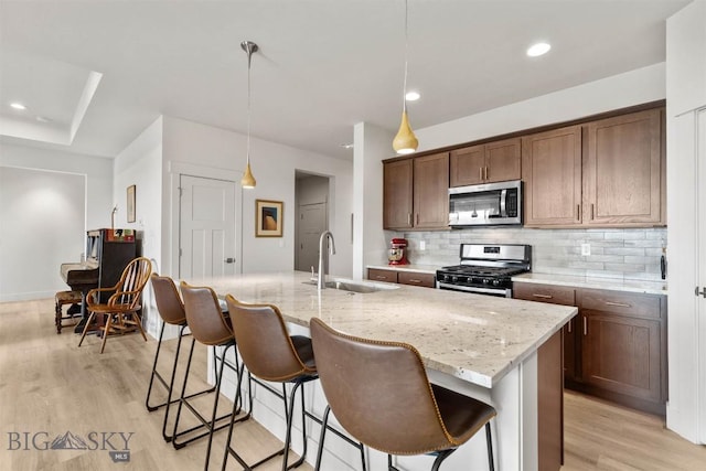 1510 Deadwood Loop, Belgrade, MT 59714 - kitchen with stainless steel appliances, decorative backsplash, light wood-style flooring, light stone countertops, and an island with sink