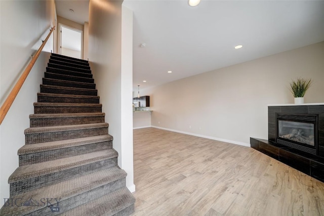stairs with a tile fireplace, baseboards, wood finished floors, and recessed lighting