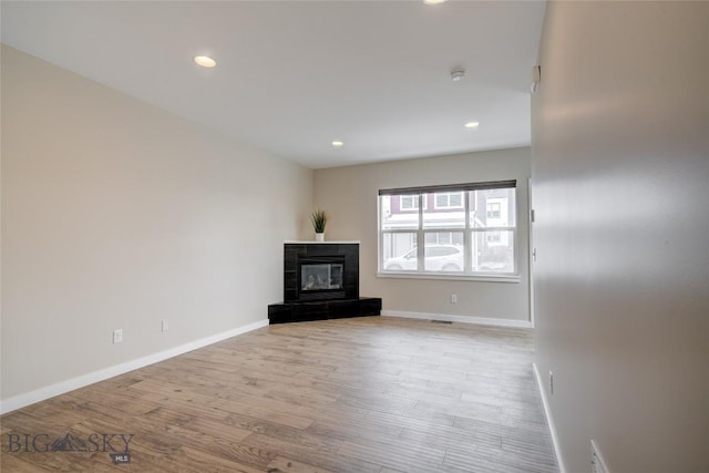 unfurnished living room featuring recessed lighting, baseboards, light wood finished floors, and a tiled fireplace