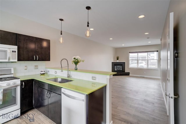 kitchen featuring light countertops, a sink, white appliances, a peninsula, and a glass covered fireplace