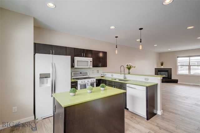 kitchen featuring a sink, a glass covered fireplace, white appliances, light countertops, and a peninsula