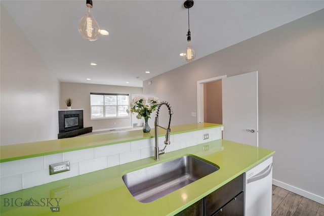kitchen featuring a sink, light wood-type flooring, dishwasher, light countertops, and decorative light fixtures