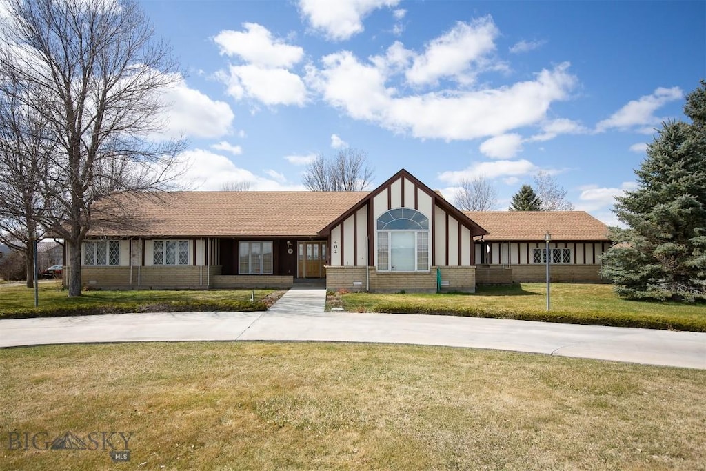 view of front facade featuring brick siding, a front lawn, and curved driveway