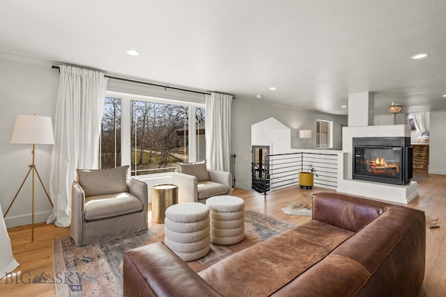living area with crown molding, wood finished floors, a multi sided fireplace, and recessed lighting