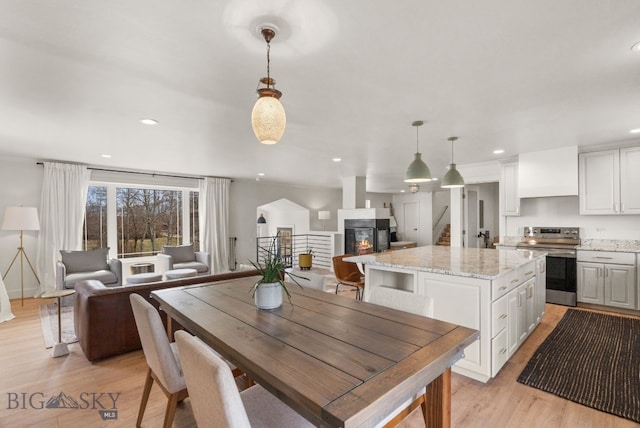 dining area featuring light wood-style flooring, recessed lighting, a glass covered fireplace, and stairs