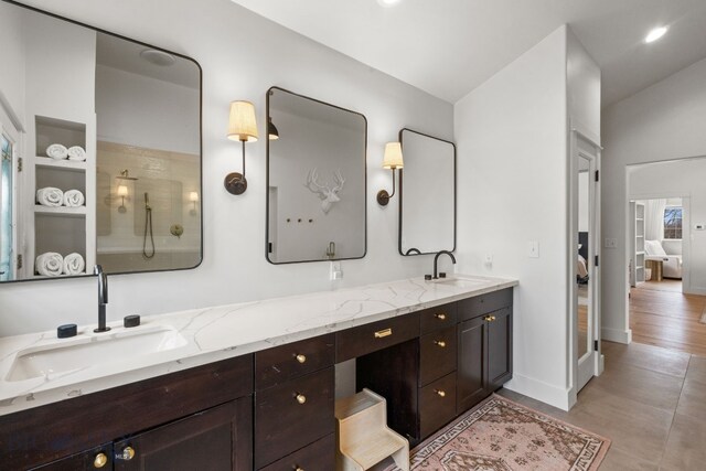 full bath with a sink, a shower, double vanity, and baseboards