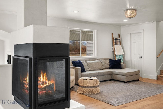 living area with ornamental molding, stairway, a multi sided fireplace, and wood finished floors