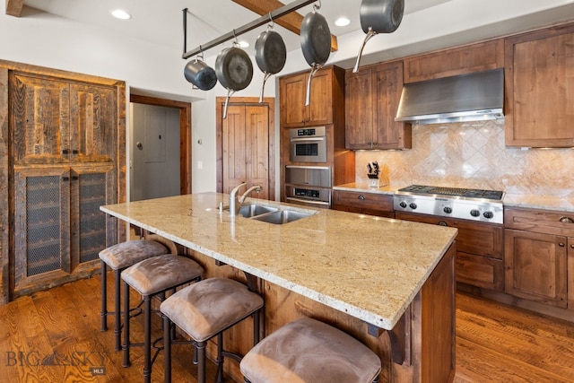 2430 Two Gun White Calf Rd, Big Sky, MT 59716 - kitchen with wall chimney range hood, a sink, stainless steel appliances, wood finished floors, and backsplash