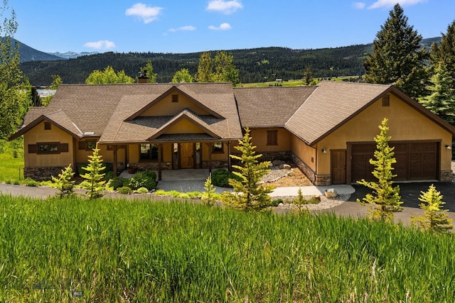 2430 Two Gun White Calf Rd, Big Sky, MT 59716 - view of front of home featuring stone siding, a garage, stucco siding, a mountain view, and a porch