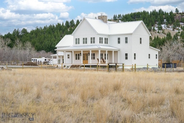 992 Deer Haven Dr, Deer Lodge, MT 59722 - back of house featuring a porch, board and batten siding, a chimney, metal roof, and a wooded view