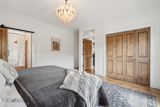 992 Deer Haven Dr, Deer Lodge, MT 59722 - bedroom with wooden walls, light wood-style flooring, a barn door, a chandelier, and a closet