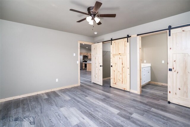 unfurnished bedroom featuring ensuite bathroom, baseboards, dark wood-type flooring, and a barn door