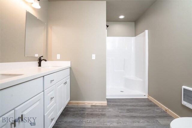 full bathroom with wood finished floors, double vanity, a sink, baseboards, and walk in shower