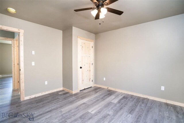 unfurnished bedroom with a baseboard radiator, baseboards, a ceiling fan, and wood finished floors