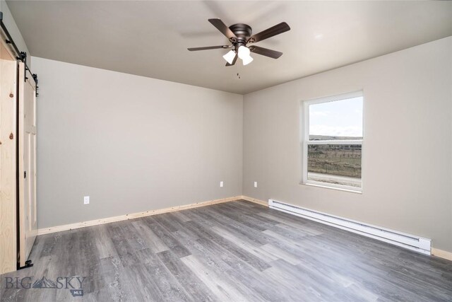 unfurnished room featuring a barn door, wood finished floors, baseboards, baseboard heating, and ceiling fan