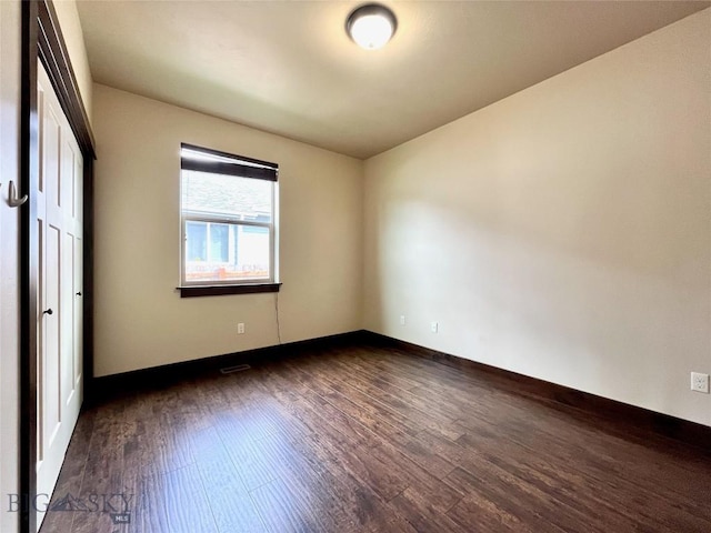empty room featuring dark wood-style flooring, baseboards, and visible vents