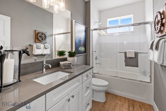 full bath featuring a notable chandelier, toilet, vanity, wood finished floors, and combined bath / shower with glass door