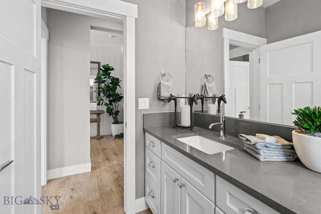 bathroom with baseboards, a notable chandelier, vanity, and wood finished floors