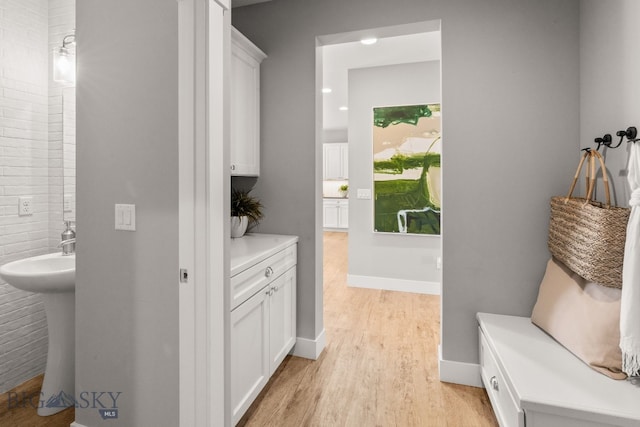 mudroom featuring a sink, baseboards, and light wood-type flooring
