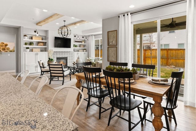 1516 Wild Bill Way, Belgrade, MT 59714 - dining area with healthy amount of natural light, a tiled fireplace, light wood-style flooring, a ceiling fan, and beam ceiling