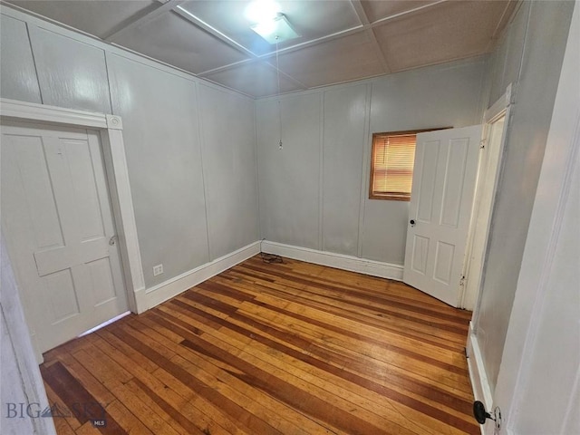 unfurnished room featuring a decorative wall, hardwood / wood-style floors, coffered ceiling, and baseboards