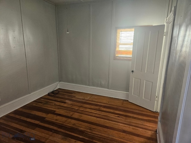 empty room featuring dark wood-style flooring, a decorative wall, and baseboards