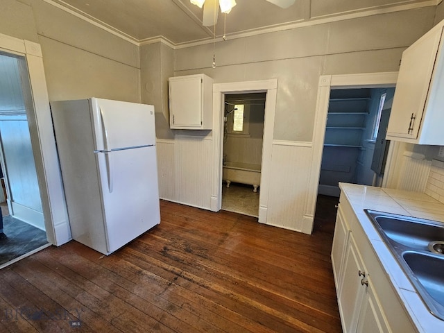 kitchen with a sink, dark wood-style flooring, tile counters, white cabinets, and freestanding refrigerator