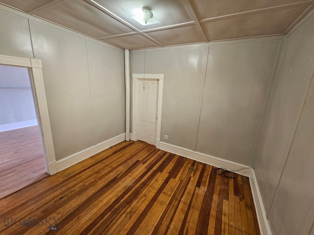 empty room with a decorative wall, hardwood / wood-style flooring, and baseboards