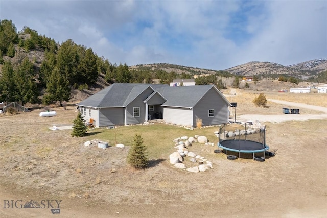 rear view of house with a trampoline, a yard, and a mountain view