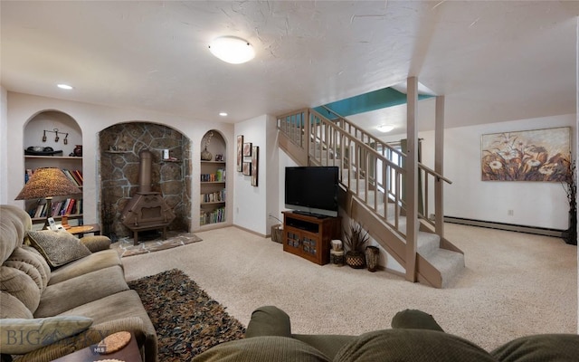 carpeted living area with built in shelves, baseboards, a wood stove, baseboard heating, and stairs