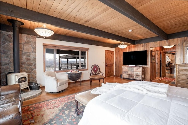 bedroom with baseboards, a wood stove, beamed ceiling, wooden ceiling, and wood finished floors