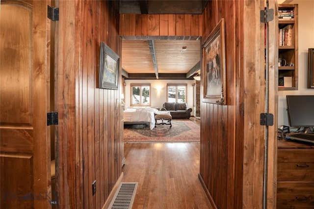 hallway featuring wood finished floors, wooden walls, and visible vents