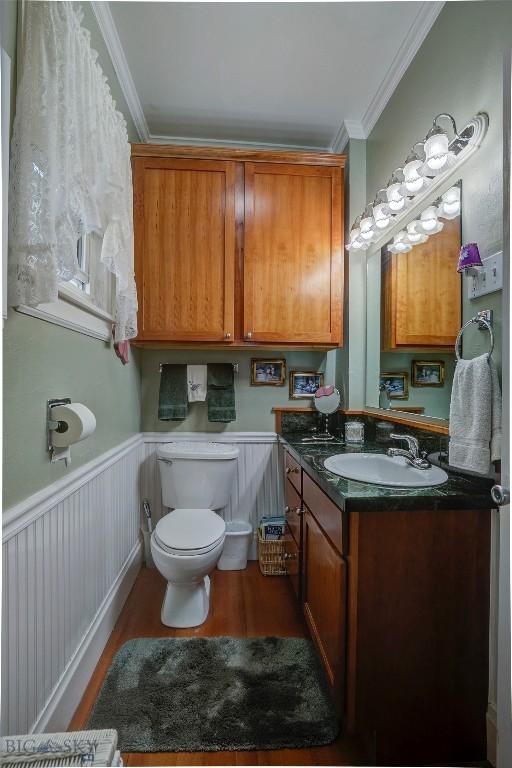half bath featuring ornamental molding, toilet, vanity, and wood finished floors