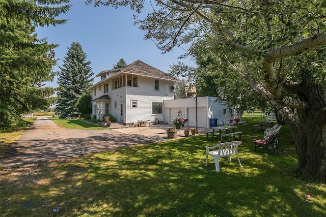 rear view of property featuring a patio, a yard, driveway, and an outdoor structure