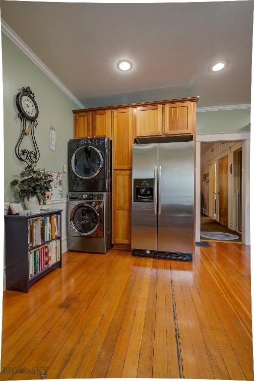 kitchen featuring crown molding, brown cabinetry, stainless steel refrigerator with ice dispenser, light wood finished floors, and stacked washer / drying machine