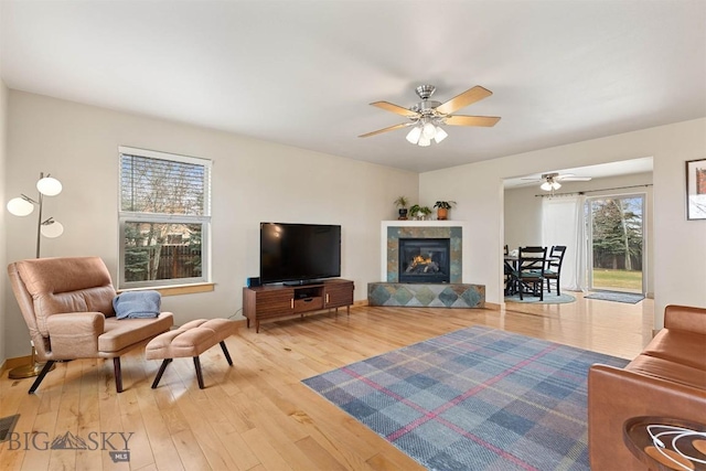 living area with a tiled fireplace, a ceiling fan, and wood finished floors