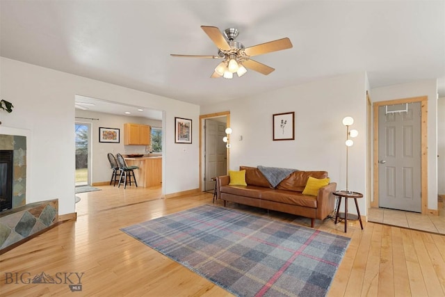 living area with a tiled fireplace, ceiling fan, light wood-style floors, and baseboards