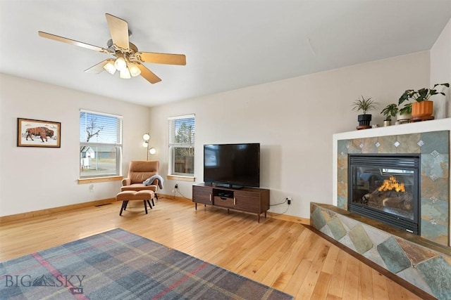 living area featuring wood-type flooring, baseboards, ceiling fan, and a fireplace