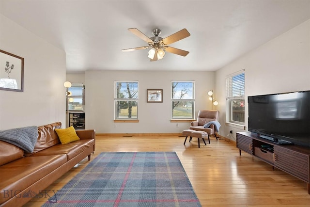 living area with light wood-type flooring, ceiling fan, and baseboards