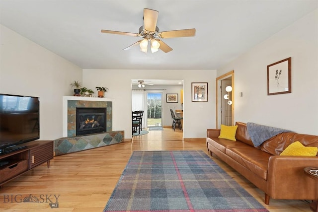 living area featuring a tiled fireplace, light wood-style floors, and ceiling fan