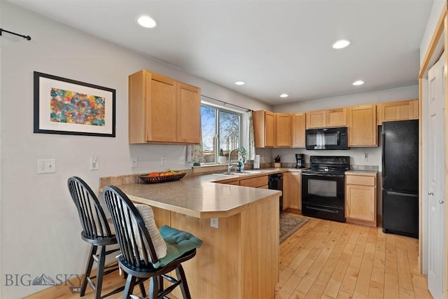 kitchen featuring a peninsula, black appliances, a kitchen bar, a sink, and light brown cabinetry