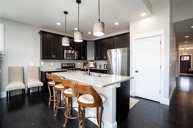 kitchen with a sink, decorative backsplash, a kitchen island with sink, appliances with stainless steel finishes, and dark wood-style flooring